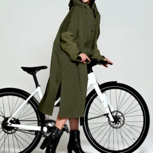 A woman in a long green "Herringbone" hooded coat and black heeled boots stands next to a white bicycle, holding the handlebars, as if she's just left a concept shop full of unique ideas. Gate21.ee
