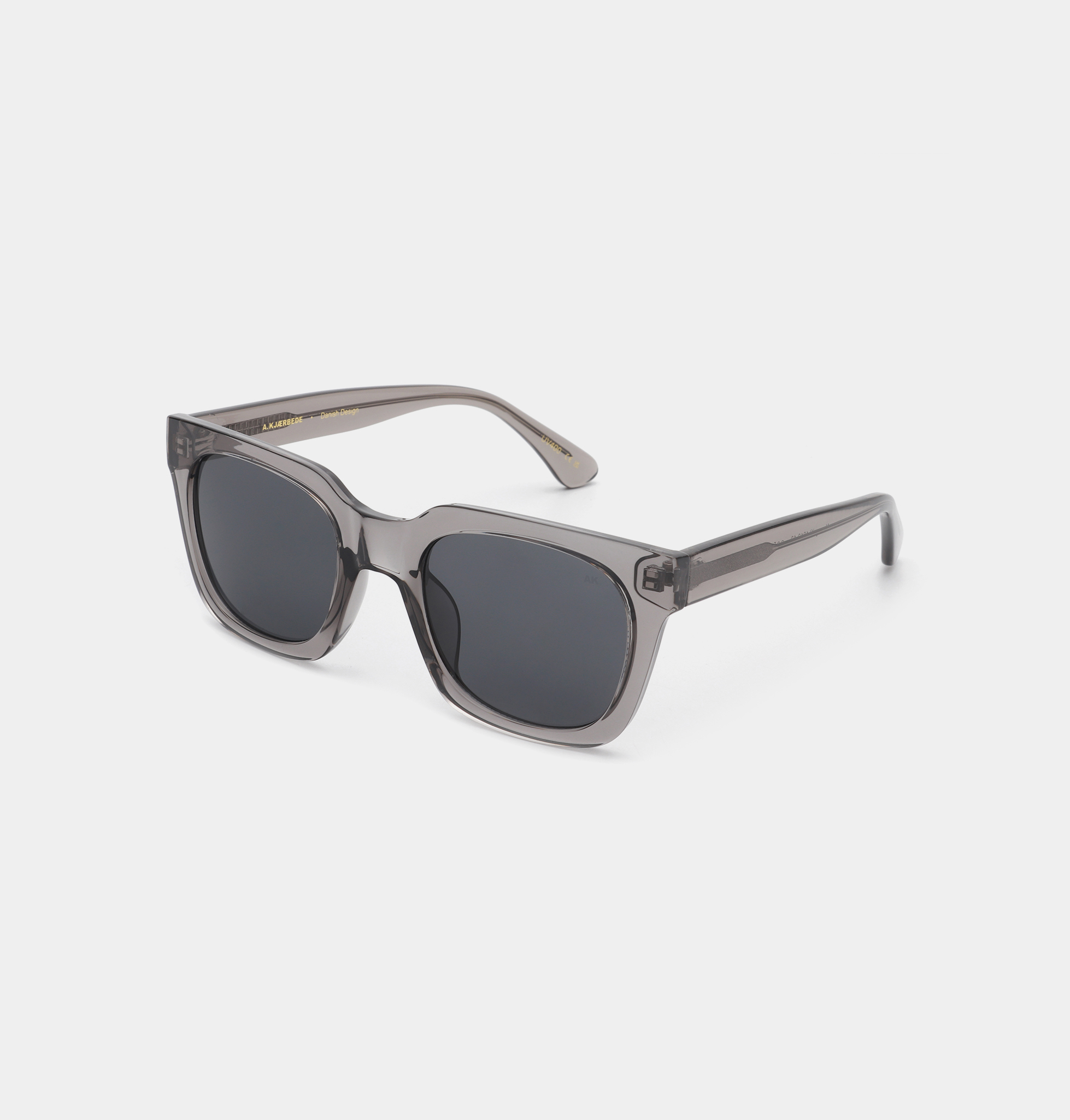 The NANCY - Grey Transparent sunglasses feature square, dark-tinted lenses and transparent grey plastic frames, exemplifying Estonian design, shown against a plain white background. Gate21.ee