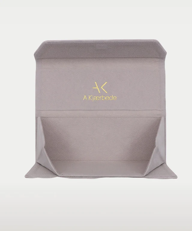 A grey, foldable A. Kjaerbede - Sunglasses Case Fold with an open flap reveals a gold logo and "A Kjaerbede" text on the soft, felt-like interior—an ideal Estonian design gift shop pick. Gate21.ee