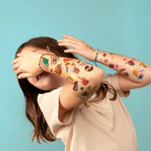 A child with long brown hair covers part of their face with tattooed arms, wearing a beige shirt against a blue background—showcasing the Surf and Skate Temporary Tattoos, ideal for any creative gift shop. Gate21.ee