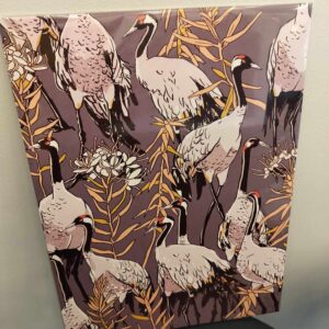 The OlevusArt Large Print&mdash;Estonian design&mdash;shows white and black cranes amid yellow and brown branches on a dark background, framed and resting against a light wall above a black chair. Gate21.ee