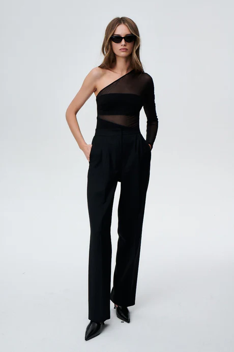 A woman poses against a plain background wearing black sunglasses, high-waisted trousers, pointed-toe shoes, and the Sex and the City Bodysuit—an elegant one-shoulder black top with a sheer panel—perfect for chic Tallinn shopping inspiration. Gate21.ee