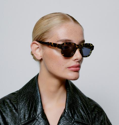 A person with slicked-back blonde hair wears HALO - Demi tortoiseshell rectangular sunglasses and a black textured jacket, facing slightly left against a light background—perfect inspiration for unique shopping in Tallinn. Gate21.ee