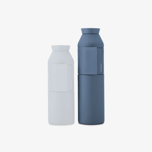The Closca Wave Large - Abyss 600ml water bottles—one light grey, one navy blue—feature minimalist, stackable designs in matte finish, bringing curated style to daily essentials. Both are shown side by side on a plain white background. Gate21.ee