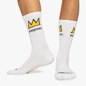 A pair of feet in Basquiat Crown - Athletic socks: white with a yellow crown and BASQUIAT below it, plus black text on the toe; this curated Estonian design stands out. Gate21.ee