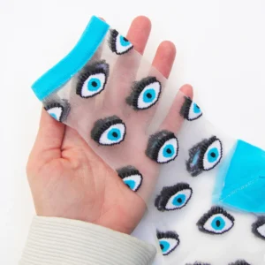 A hand displays the Blue Eyes – Transparent Socks, featuring a sheer design with bright blue toe and cuff, and a repeating pattern of blue and black eye illustrations—a unique accessory inspired by Estonian style for concept shop shoppers. Gate21.ee