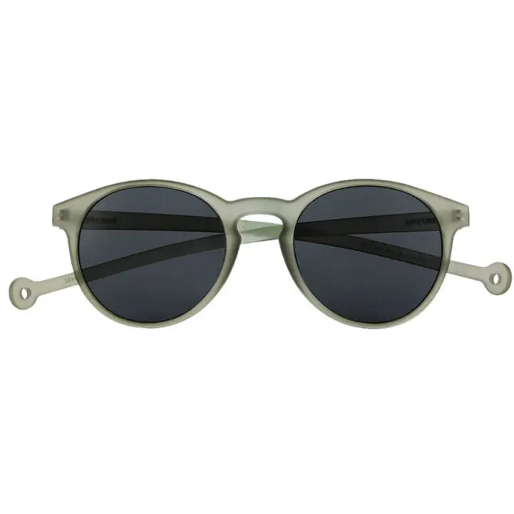 The "Isla" Moss Sunglasses feature round, grey frames with black lenses, small circular holes near the temple ends, and a matt finish—a distinctive Estonian design perfect for any gift shop seeking unique items. Gate21.ee