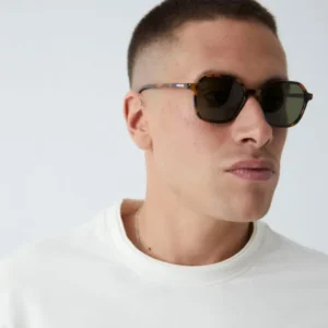 Wearing short hair and a plain white crew-neck shirt, a person looks aside against a neutral background, showcasing "Valle" Tortoise Sunglasses—a style often seen in Tallinn concept shops featuring Estonian design. Gate21.ee
