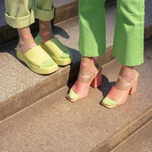 Two people on stone steps highlight Estonian design, wearing light green trousers and pastel sandals with Sakura - Transparent Socks featuring pink and yellow flower patterns. Gate21.ee