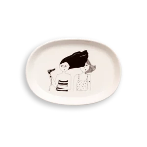 The Bathroom - Tray is an oval white ceramic plate with a black and white illustration of two women, one holding a hairdryer and blowing the other's hair—a standout piece for unique gift shop finds. Gate21.ee
