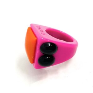 The Agatka - Ring is a chunky pink plastic accessory with a bold orange rectangle on top and two round black accents, ideal for anyone seeking standout pieces in a curated gift shop selection. Gate21.ee