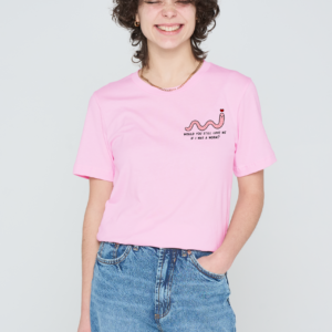 A person with short curly hair smiles with eyes closed, wearing the pink Love Me Worm T-Shirt featuring a small worm graphic and text, paired with blue jeans, standing against a plain light background. Gate21.ee