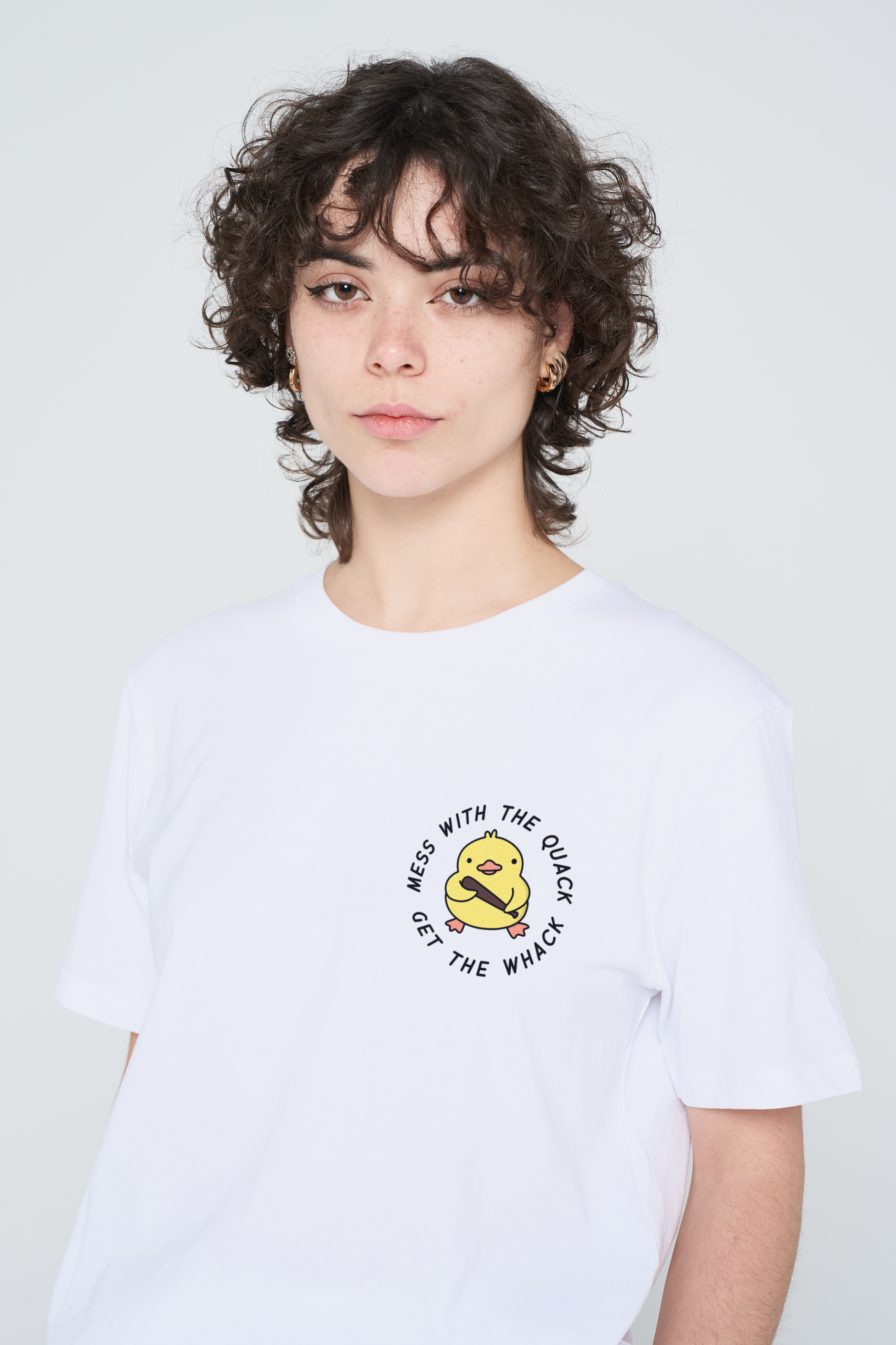 A person with short, curly brown hair wears a pink Love Me Worm T-shirt featuring a cartoon duck and the text “MESS WITH THE QUACK GET THE WHACK” printed on the front. The background is plain light grey. Gate21.ee