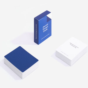 A blue box labelled Journal Prompt Cards rests on a white surface, beside two curated stacks—one with a blue lined back and one showing a white front with printed prompts—ideal for gift shops or concept stores. Gate21.ee