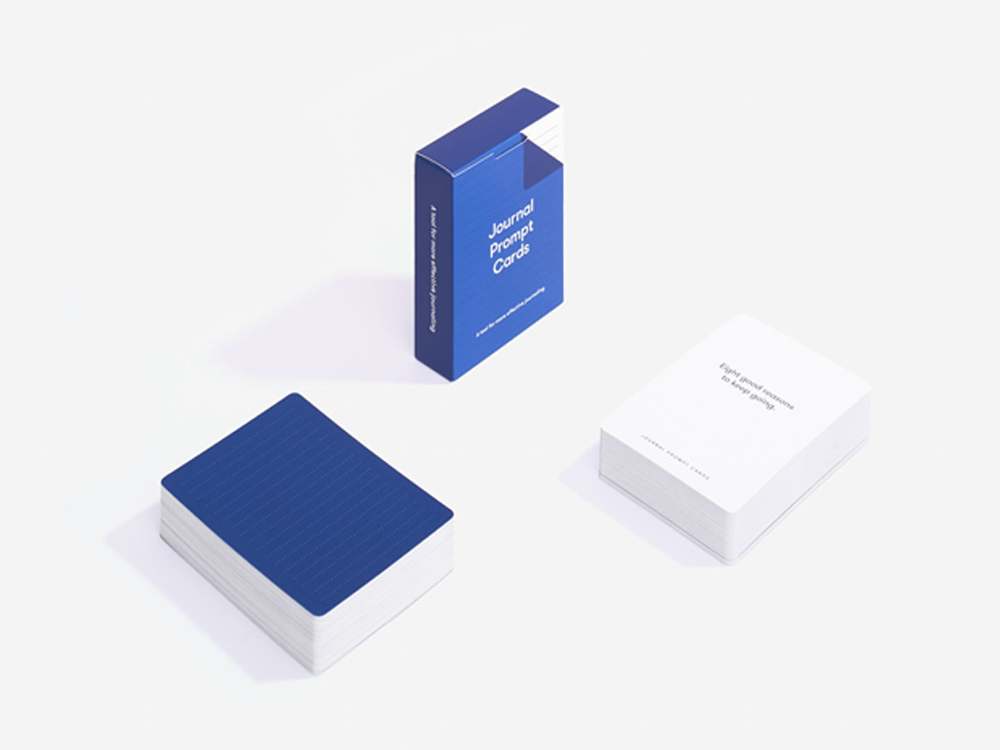 A blue box labelled Journal Prompt Cards rests on a white surface, beside two curated stacks—one with a blue lined back and one showing a white front with printed prompts—ideal for gift shops or concept stores. Gate21.ee