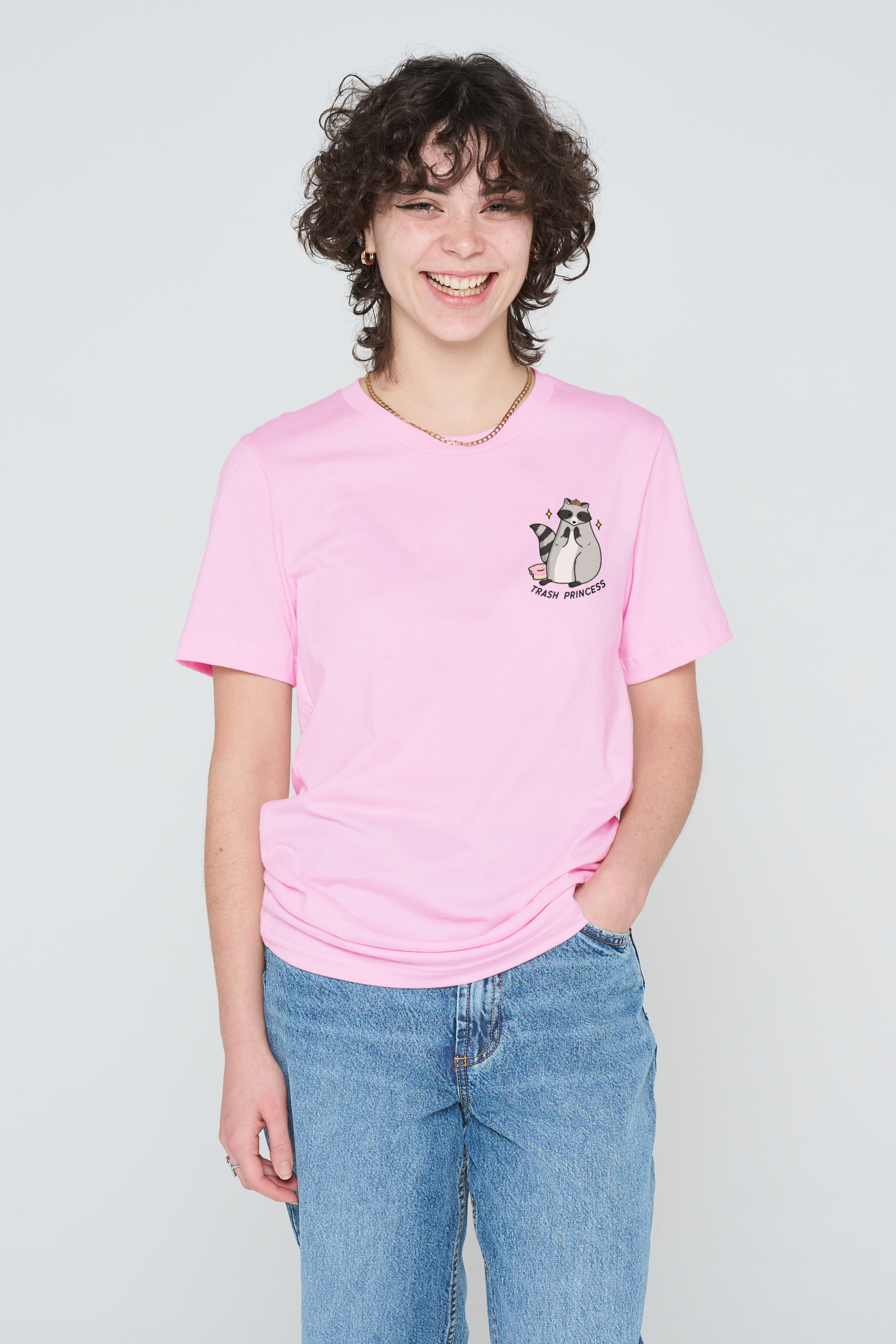 A person with curly hair smiles at the camera, wearing a light pink Love Me Worm T-shirt and blue jeans, with one hand in their pocket. Gate21.ee