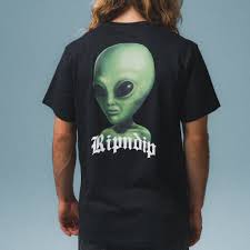 A person with long hair sports the We come in Peace Tee - Black, which features a large green alien face and "Ripndip" in bold white lettering on the back, capturing the curated style typical of a concept shop. Gate21.ee