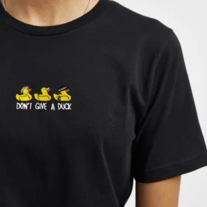 Person wearing a black t-shirt with three cartoon yellow ducks embroidered on the chest, each with a different accessory, and text below them reading “DON’T GIVE A DUCK.” A fun, curated find perfect for Tallinn shopping or your favourite gift shop. Gate21.ee