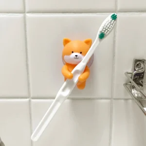 The Sloth - Toothbrush Holder, a fun orange animal shape with a suction cup, holds a white toothbrush on your tiled bathroom wall—adding playful style and creative charm to daily routines. Gate21.ee