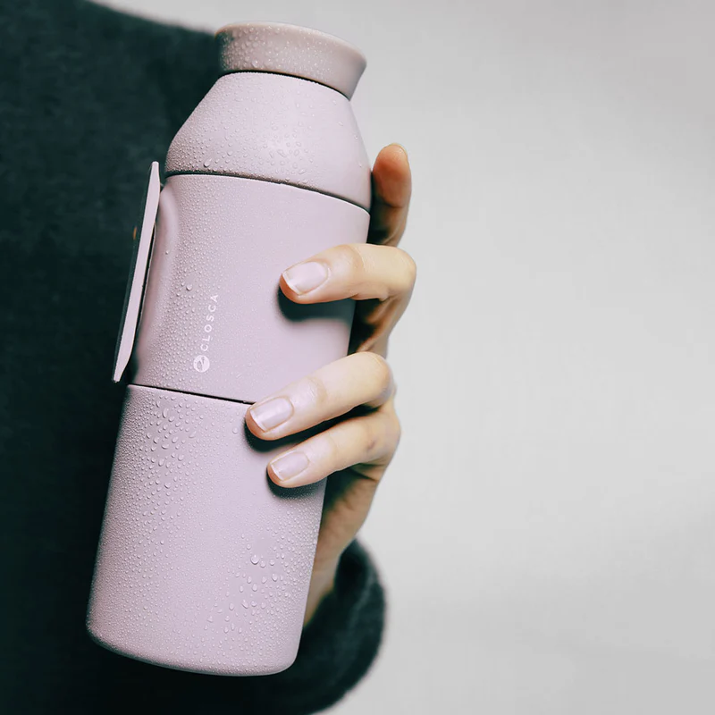 A hand holds the Closca Wave – Himalaya 600ml reusable water bottle, its mauve surface beaded with condensation—an Estonian-designed find ideal for Tallinn shopping or as a unique present. Gate21.ee