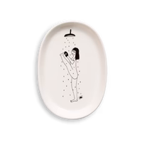 The "Yoga in the Shower - Tray" is an oval white plate from a curated Estonian design shop, featuring a black line drawing of a person raising one leg under a shower with water droplets falling. Gate21.ee