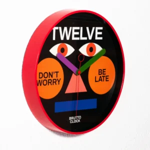 The BE LATE - Wall clock, with its red frame and graphic face featuring eyes, an orange nose, and mouth, highlights Estonian design and playful text&mdash;making it a unique addition to any gift shop collection. Gate21.ee