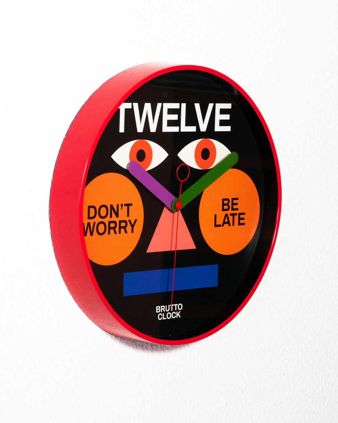The BE LATE - Wall clock, with its red frame and graphic face featuring eyes, an orange nose, and mouth, highlights Estonian design and playful text—making it a unique addition to any gift shop collection. Gate21.ee