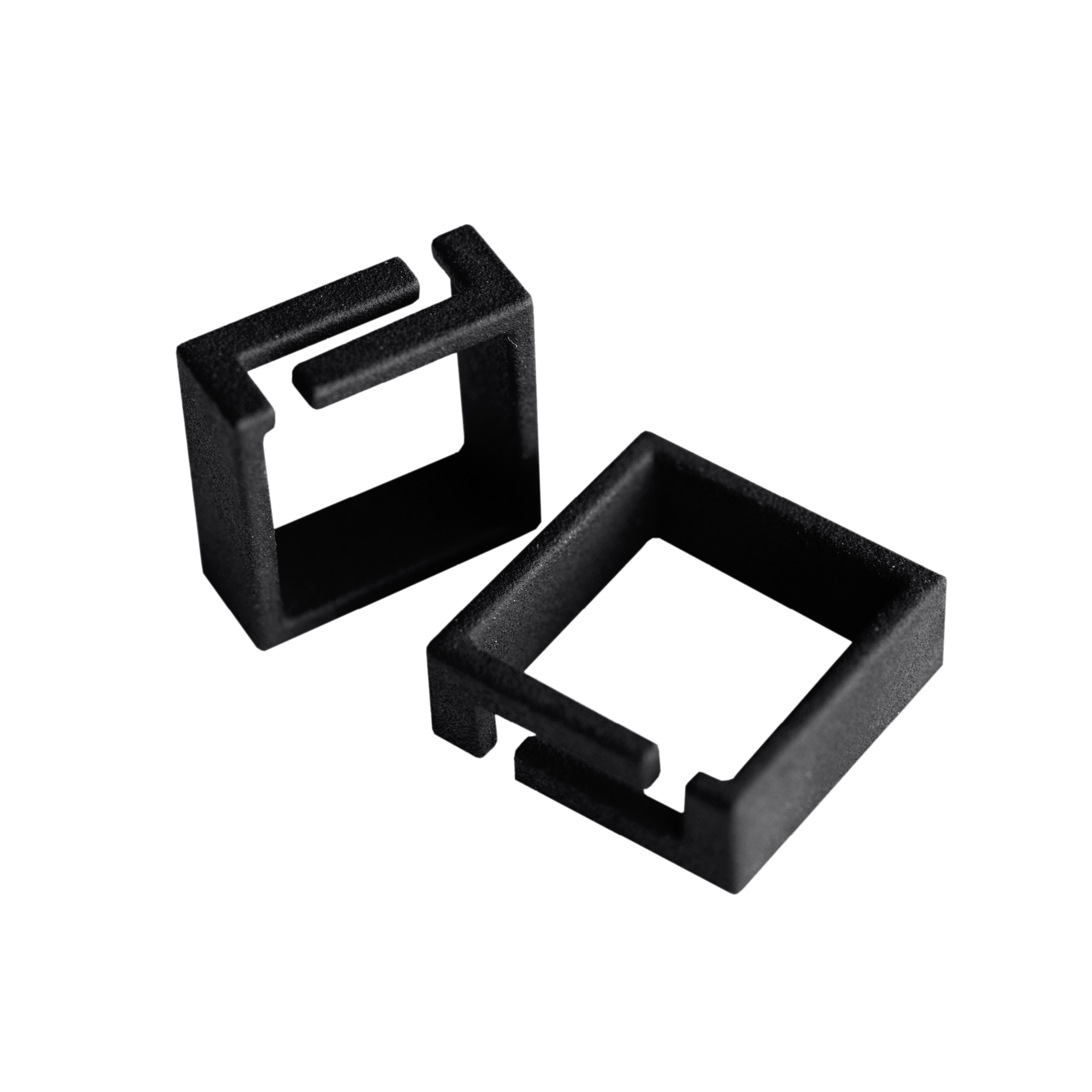 Two small, black, square-shaped plastic clips with open sides are positioned on a white background—stylish accessories you might find in a Tallinn shopping concept shop. One clip stands upright whilst the other lies flat. Gate21.ee
