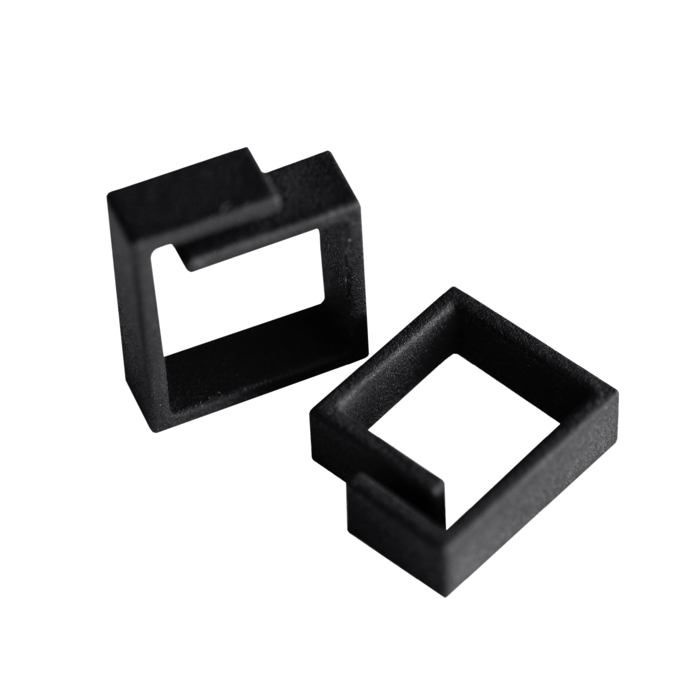 Two black, geometric, open rectangular shapes made of a solid material are positioned on a white background, showcasing the minimalist aesthetic of Estonian design; perfect for those interested in curated Tallinn shopping. Gate21.ee