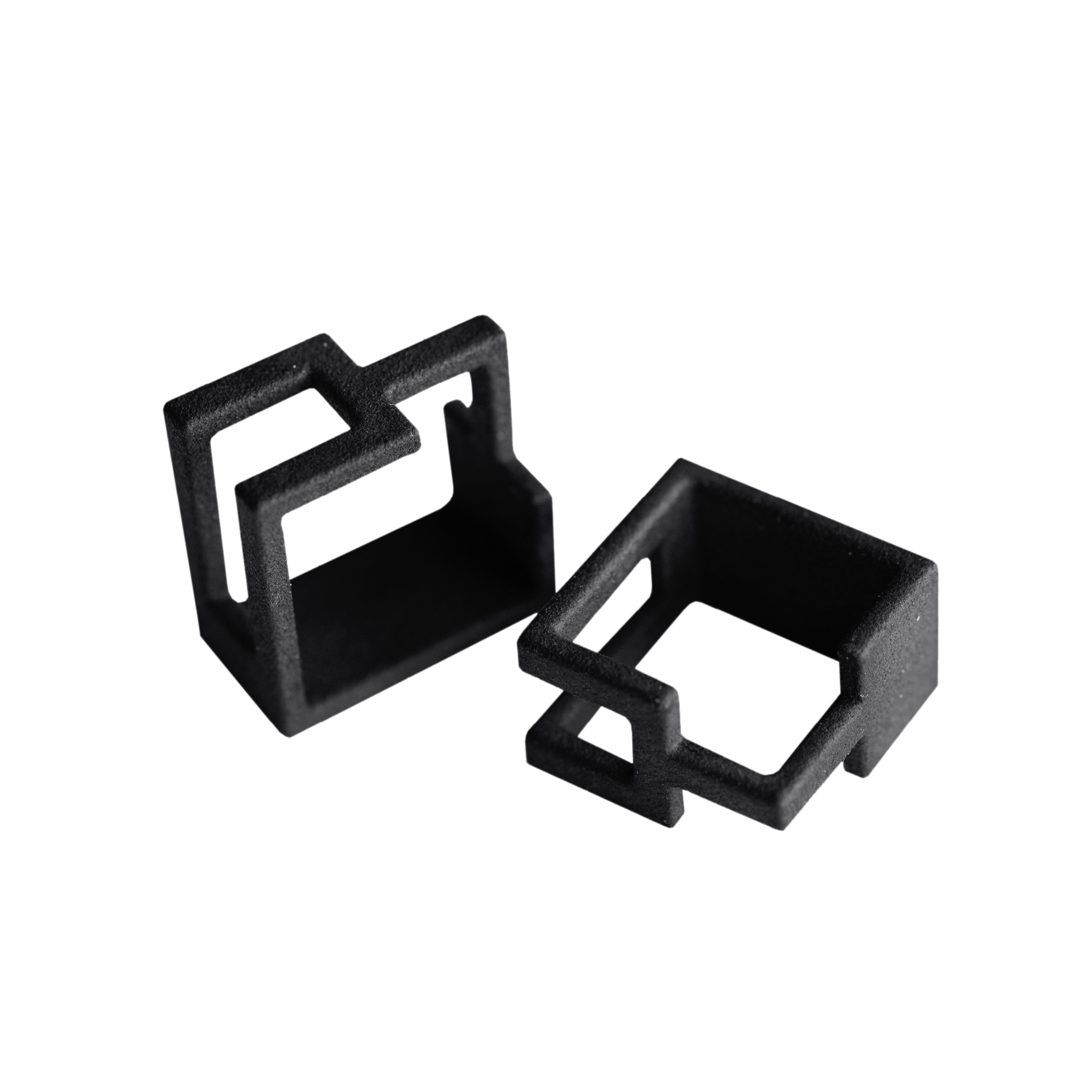 Two small, black, rectangular plastic components with geometric cut-outs rest on a white background. Their precise shapes reflect Estonian design—perfect for those seeking unique ideas or memorable finds from Tallinn shopping. Gate21.ee