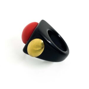 The Doris - Ring features a bold black band topped with a large round red dome and accented by a gold circle on the side, showcased against a white background—an eye-catching example of Estonian design. Gate21.ee