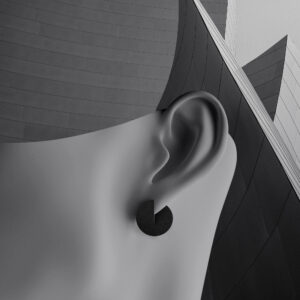 Close-up of a minimalist, greyscale sculpture of a human ear wearing a geometric black earring, set against modern, angular architecture—a curated scene that sparks unique ideas in contemporary design. Gate21.ee