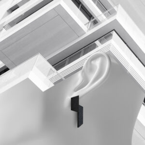A geometric black earring is worn on a smooth, stylised white ear, set against the angular lines of a modern building—an aesthetic perfect for a concept shop seeking unique ideas in monochrome design. Gate21.ee