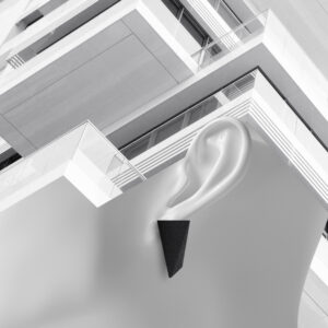 A mannequin ear wearing a black triangular earring—a nod to Estonian design—is positioned before the exterior of a modern building with angular balconies. The image is in black and white, evoking the feel of a curated concept store display. Gate21.ee