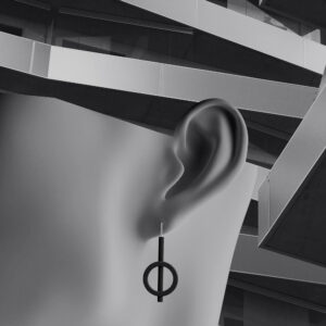 A close-up of a mannequin’s ear wearing a geometric earring shaped like a circle intersected by a vertical bar, set against an abstract, angular building—perfect for those seeking curated style from a concept shop. Gate21.ee