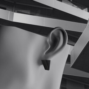 A close-up of a smooth, abstract human ear wearing a black triangular earring, with curated geometric, layered architectural elements in the background. The image is in greyscale. Gate21.ee