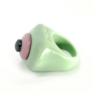The Fluffy Mint - Ring is a chunky, pastel green resin piece with a glossy finish, featuring a raised round pink accent, a small black circle on top, and an engraved brand name—showcasing unique Estonian design. Gate21.ee