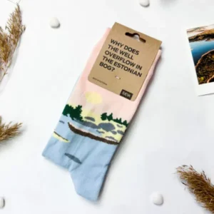 Eesti sokid – Tule saarele sa! feature a scenic print of water, trees, and a canoe, with a tag reading "WHY DOES THE WELL OVERTOWN IN THE ESTONIAN BOG?" Perfect Tallinn gift; displayed on white with photos and dried plants nearby. Gate21.ee
