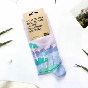 A pair of Eesti sokid – mine rappa! socks with a scenic design is displayed on a flat surface, surrounded by photos and plants—a unique gift or Tallinn shopping find. The tag asks, “What do you need to find on the islands of Estonia?”. Gate21.ee
