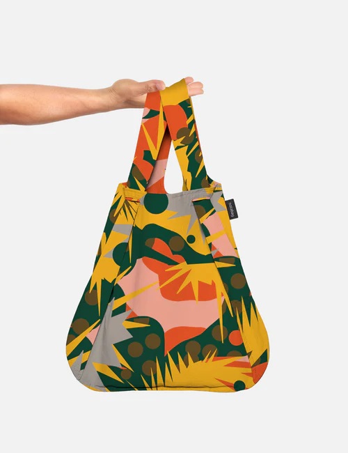 A hand holds Spark, a reusable shopping bag with an abstract pattern in green, yellow, and orange. With two handles and a small black tag, this stylish accessory is ideal for Tallinn shopping or trips to your favourite concept store. Gate21.ee