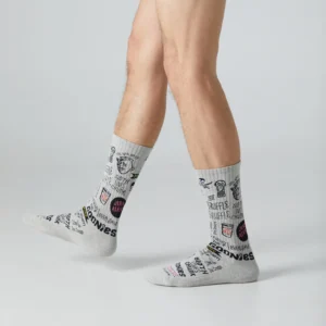 A person with light skin stands on a grey surface wearing Goonies 4 Life - Athletic socks featuring black and red doodles, text, and cartoon graphics. Only the legs and feet are visible—perfect for fans of unique, trendy gift items. Gate21.ee