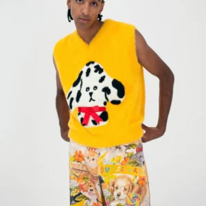 A person stands against a white background wearing the Manolito Vest&mdash;a bright yellow sleeveless top with a cartoon dog and red bow, showcasing playful Estonian design&mdash;paired with colourful shorts decorated with dogs, flowers, and "OUTSIDER. Gate21.ee