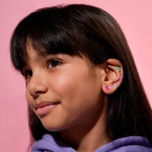 A young girl with straight dark hair and a fringe wears Lily - Earring Stickers, featuring curated, colourful designs on her ear. She is dressed in a lavender hoodie against a pink background. Gate21.ee