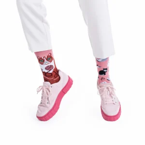 A person stands against a white background wearing white trousers and light pink trainers with thick pink soles, paired with Playful Cats mismatched pink socks featuring cat designs inspired by Estonian design. Gate21.ee