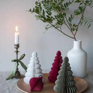 A curated display features a white candle in a metal holder, Paper Christmas Trees - 30cm - KÕIK in festive colours, and a white vase with green branches on a wooden tray—ideal inspiration for Tallinn shoppers or fans of Estonian design. Gate21.ee