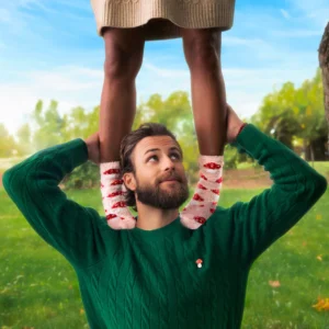 A man in a green jumper holds a child wearing Mushroom - Fuzzy Socks and a beige skirt on his shoulders as they enjoy time together in a grassy park with trees and blue sky in the background. Gate21.ee