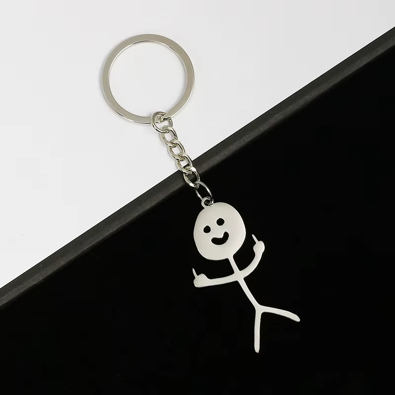 The Zen - Keyring Man - KÕIK is a metal keyring featuring a smiling stick figure holding up both middle fingers, set against a diagonally split black and white background—a bold Estonian design available in Tallinn concept shops. Gate21.ee