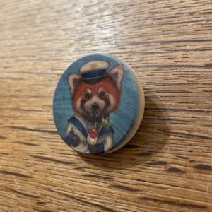 The Proverb Puidust Prossid - K&Otilde;IK is a round wooden badge featuring a red panda in a sailor hat and uniform holding a flower&mdash;an ideal, unique find for anyone exploring Tallinn&rsquo;s curated shopping treasures. Gate21.ee