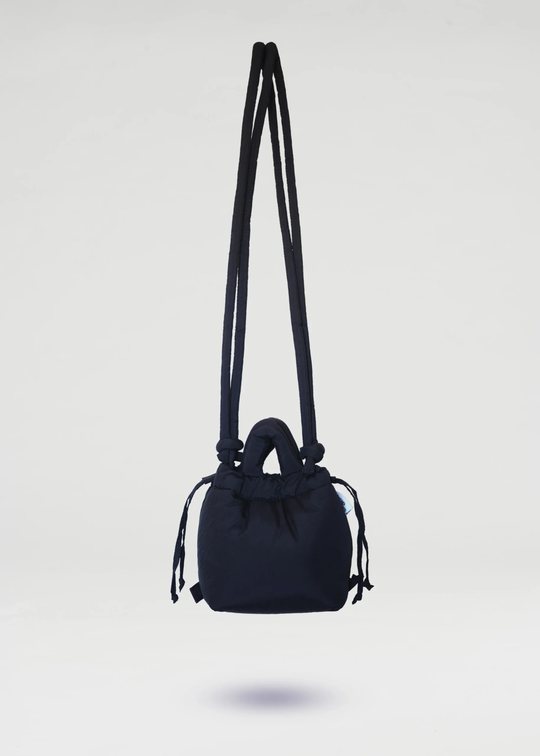 The Micro Ona Soft Bag - Black is a compact fabric shoulder bag with two long straps, a short handle, and drawstring details on both sides—an ideal curated piece for any concept shop, shown suspended against a plain white background. Gate21.ee