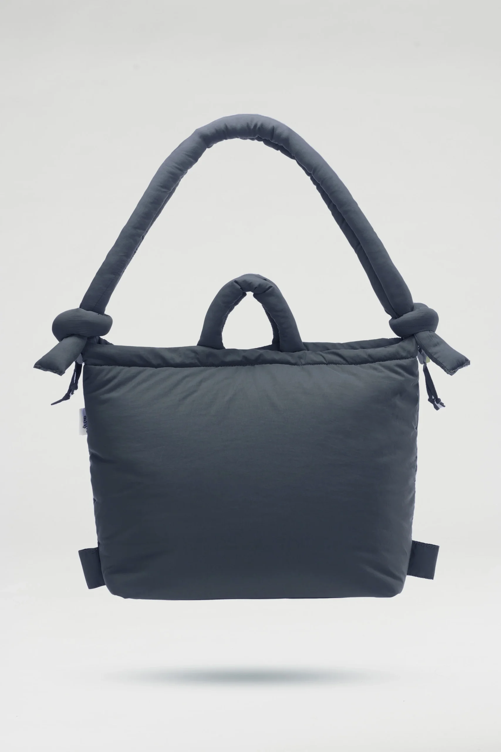 The Ona Soft Bag - Coal is a dark grey padded tote with one large knotted handle and one small handle, shown on a plain background—ideal for your next Tallinn shopping trip or as a striking addition to your concept shop collection. Gate21.ee